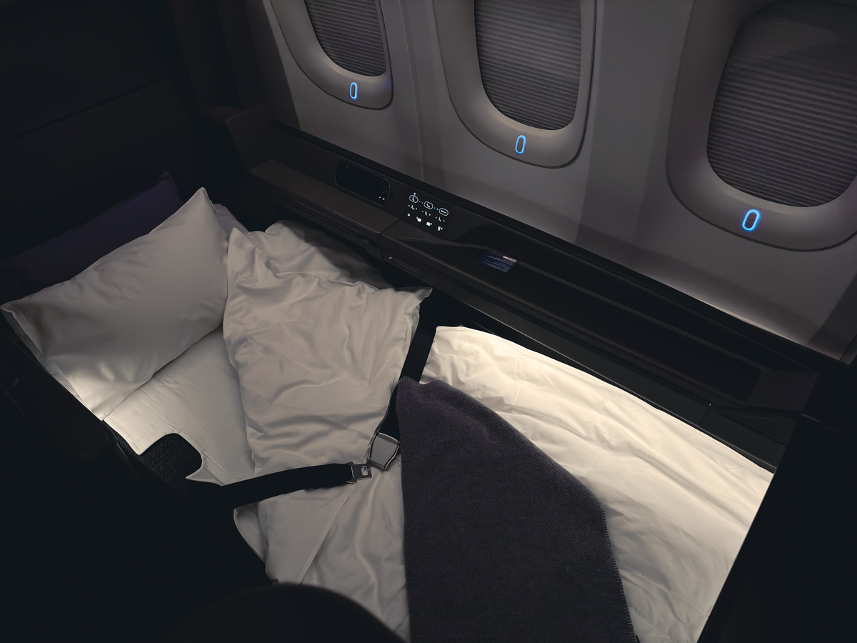 ANA First Class seat turned into a bed with sheets and pillow.